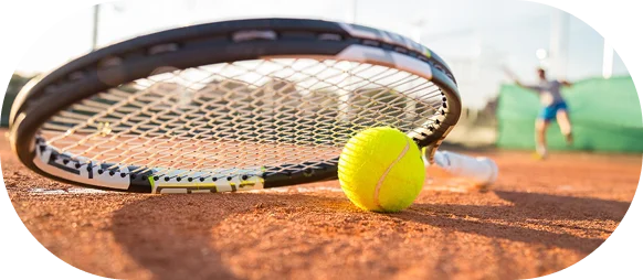 Raquete de ténis e bola deitadas num court de ténis de terra batida durante uma sessão de treino